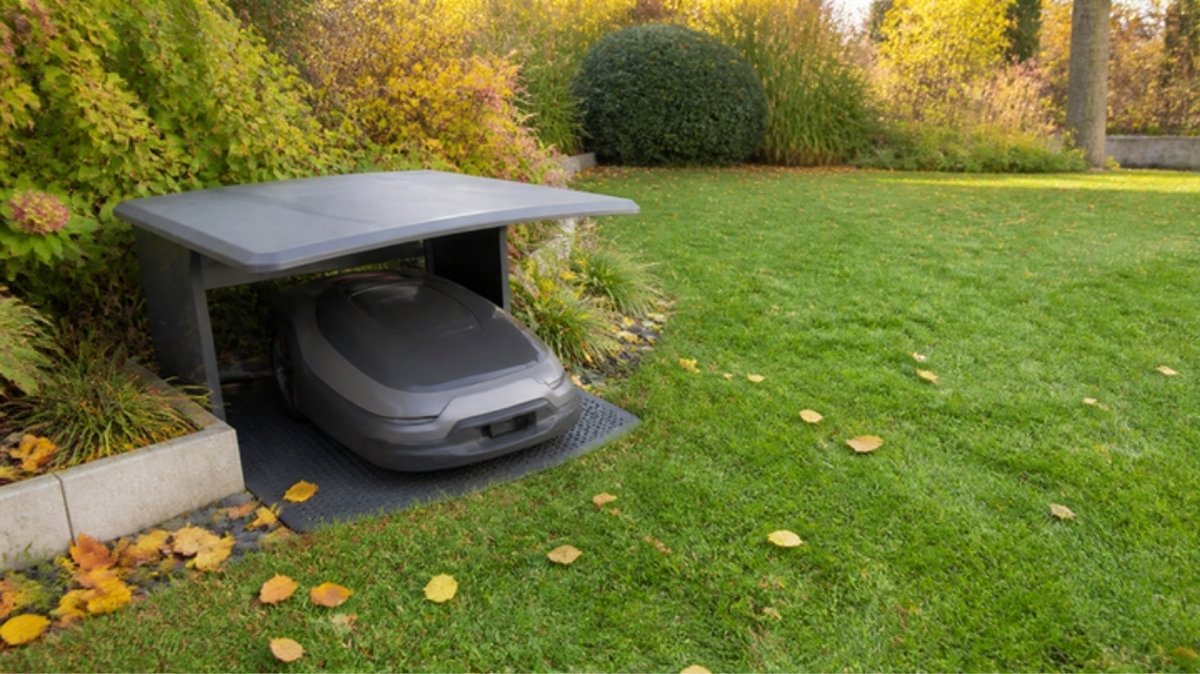 Mähroboter in einer Garage am Rand des Rasens (Symbolbild, KI-generiert)